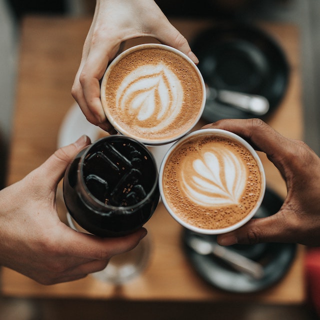 three hands "cheersing" with cups of coffee, two cappuccinos and one iced coffee in a glass mason jar. If you're looking for a great morning coffee in Ko Olina, look no further than Hokulea Cafe.