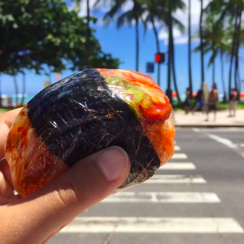 hand holding kimchi musubi in front of a street. If you're looking for convenient, authentic local bites while in Ko Olina, look no further than Island Country Markets.