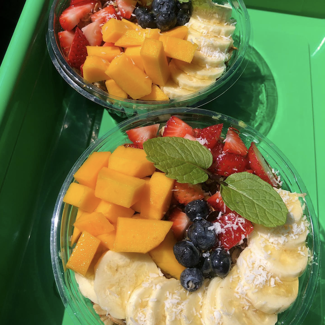 pair of acai bowls from Lanai Wai Juice, one of the best Lanai restaurants, topped with straberries, blueberries, apple bananas, fresh local mangoes, and a sprig of mint, set on a bright green wagon